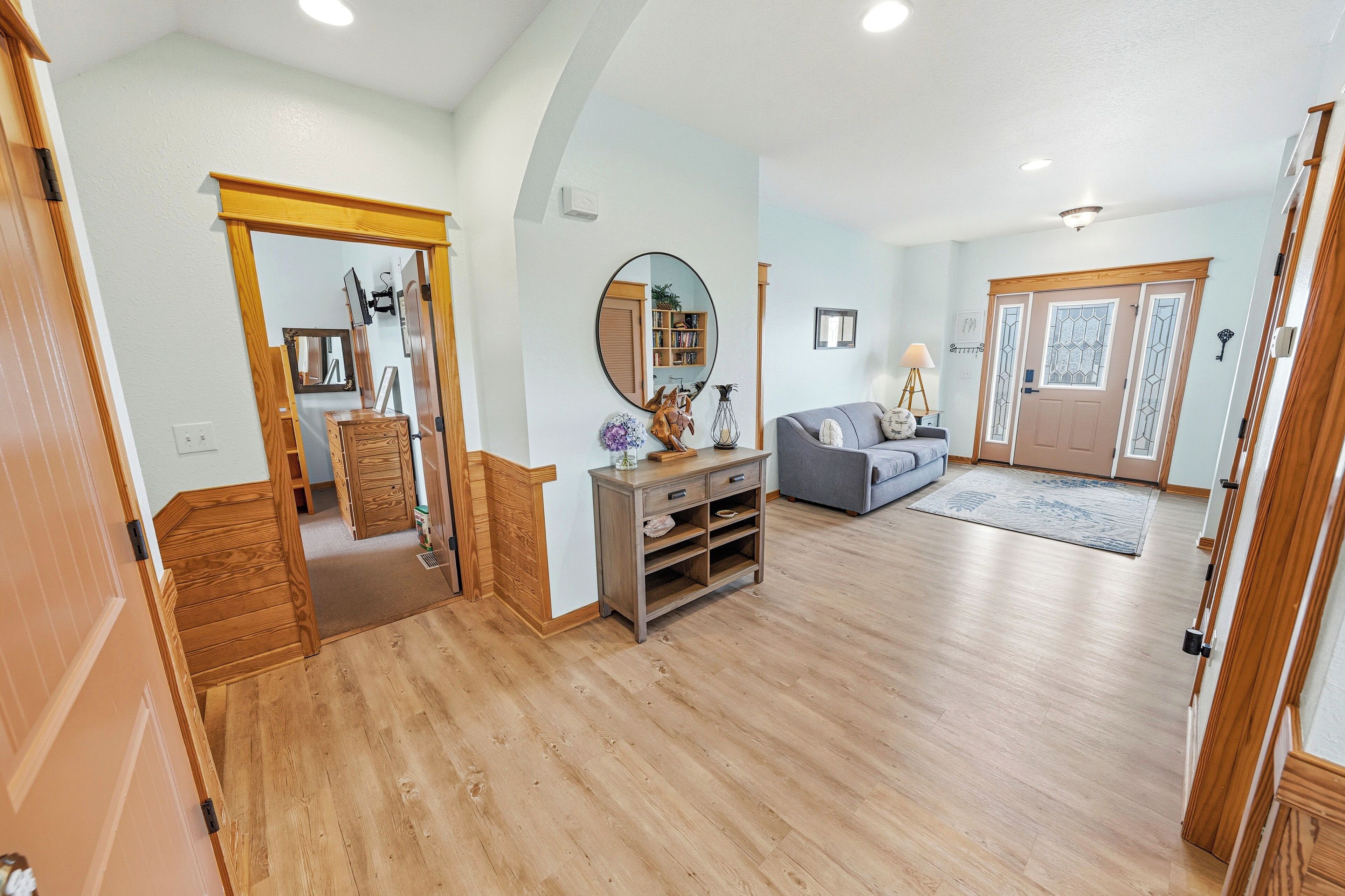 A spacious living room with hardwood flooring, a gray sofa, a wooden console table, and a mirror.