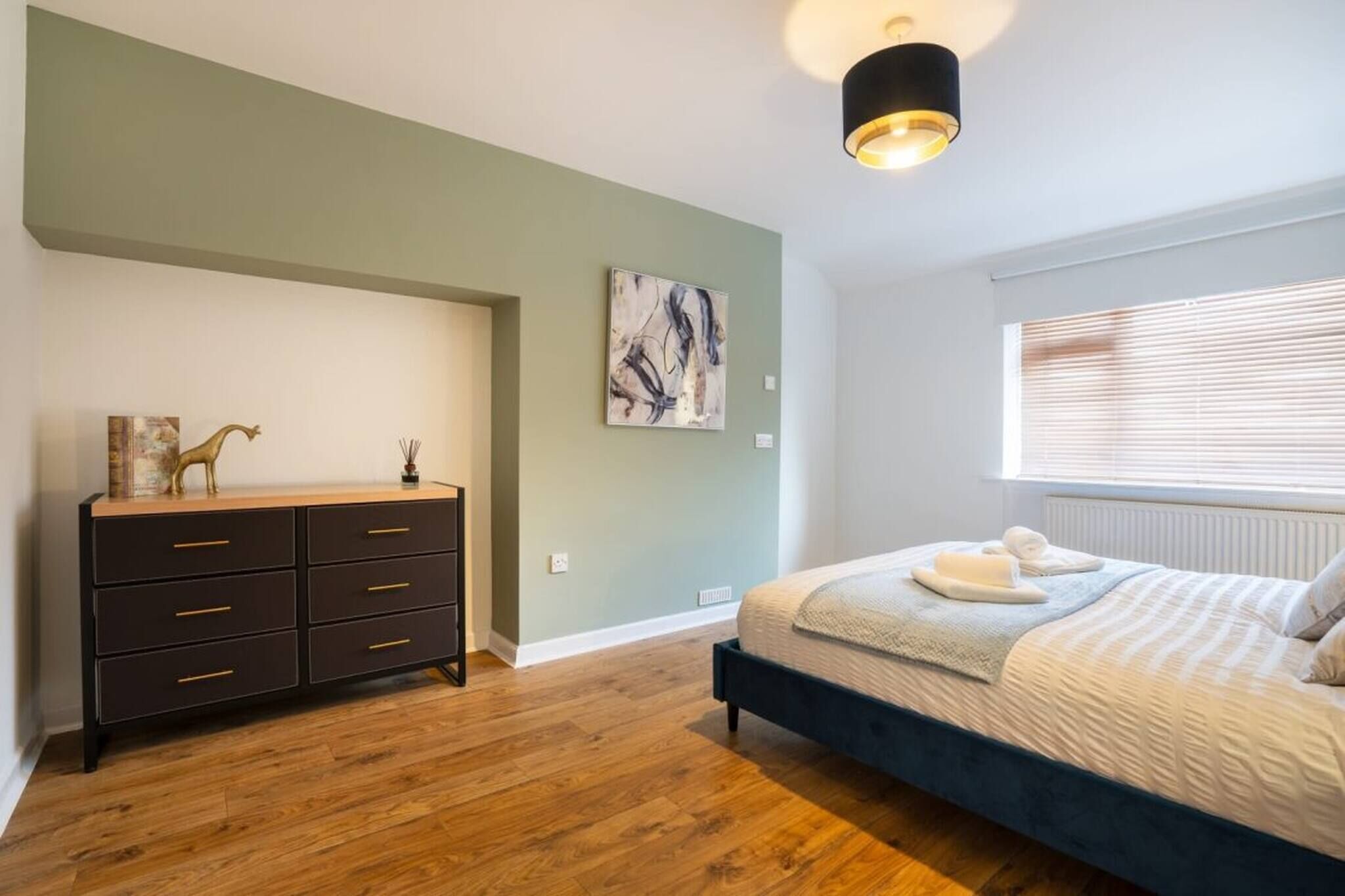 A bedroom with a bed, a dresser, a painting, and a window with blinds.