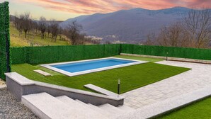 Ein rechteckiger Pool mit einer umgebenden Pflasterfläche und einem grünen Heckenstreifen.