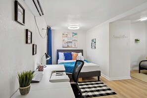 Ein modernes Hotelzimmer mit einem ordentlich bezogenen Bett, einem Schreibtisch mit Computer, einem Stuhl und einer kleinen Topfpflanze.
