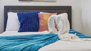 Ein ordentlich bezogenes Bett mit einer blauen Decke, einem weißen Kopfkissen und einem blauen, strukturierten Kissen.