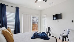 Een slaapkamer met een bed, een televisie, een plafondventilator en een openslaande balkondeur.