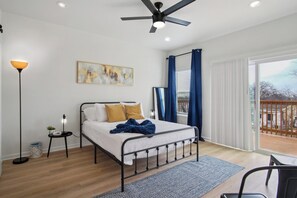 A bedroom with a bed, a floor lamp, a painting, a ceiling fan, and a view of the outdoors. - Minutes to Downtown: Spacious 4BR/3BA Historic Gem (San Antonio)