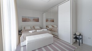 Une chambre à coucher moderne avec un lit, des tables de chevet, un banc, un miroir et des œuvres d’art accrochées au mur.