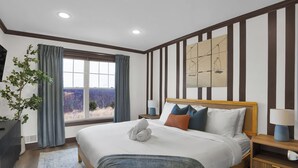 Una habitación de hotel moderna con una cama grande, vistas al exterior, un cabecero de madera y una mesita de noche con lámpara.