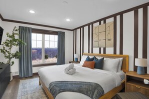 A modern hotel room with a large bed, a view of the outdoors, a wooden headboard, and a nightstand with a lamp. - Luxury Camelback Summit: 5bed 4bath, Hot Tub, Game Room, Movie Room, Slope Views (Tannersville)