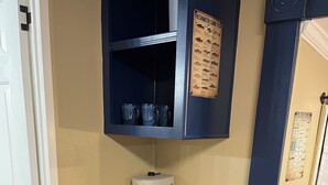 Uma cozinha compacta com cafeteira, chaleira e uma prateleira com canecas.