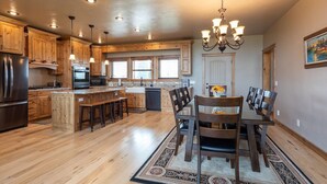 A spacious kitchen with wooden cabinets, a stainless steel refrigerator, and a dining area with a chandelier. - Teton View Retreat- Hot Tub - Game Room - Fire Pit (Alta)