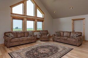 A spacious living room with two brown leather sofas, a patterned rug, and large windows offering a view of the outdoors. - Teton View Retreat- Hot Tub - Game Room - Fire Pit (Alta)