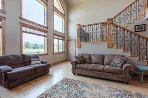 Ein geräumiges Wohnzimmer mit zwei braunen Ledersofas, einem gemusterten Teppich und einer Holztreppe mit aufwendigen Metallgeländern.