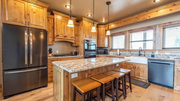 A kitchen with wooden cabinets, stainless steel appliances, a granite countertop, and bar stools. - Teton View Retreat- Hot Tub - Game Room - Fire Pit (Alta)