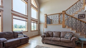 A spacious living room with two brown sofas, a patterned rug, and a wooden staircase with a wrought iron railing. - Teton View Retreat- Hot Tub - Game Room - Fire Pit (Alta)