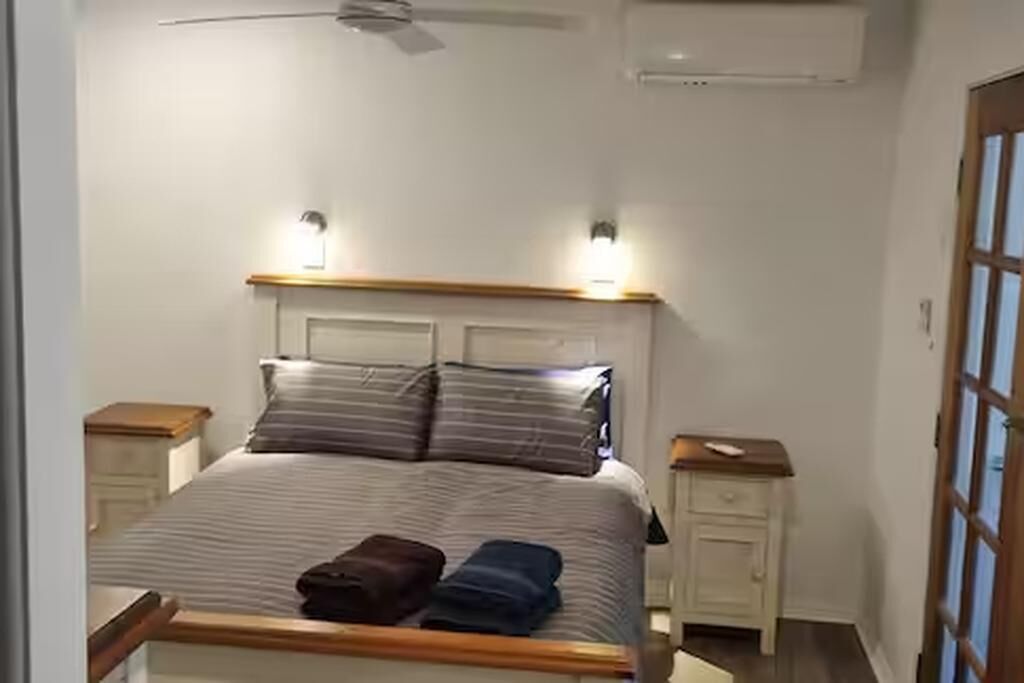 A neatly made bed with striped bedding and two pillows, a bedside table with a lamp, and a ceiling fan.