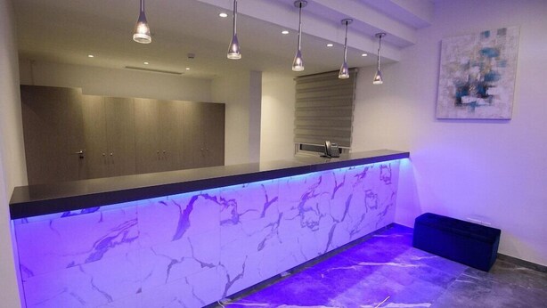A modern reception area with a marble counter, pendant lighting, and a large abstract painting on the wall. - Annex Apartments (Ayia Napa)