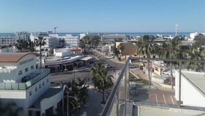 A coastal cityscape with modern buildings, palm trees, and a clear blue sky. - Annex Apartments (Ayia Napa)