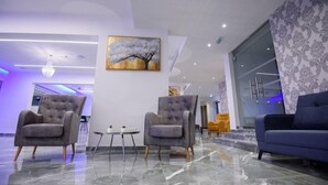 A modern lobby with marble flooring, two grey armchairs, a small table with a vase, and a large painting of a tree. - Annex Apartments (Ayia Napa)
