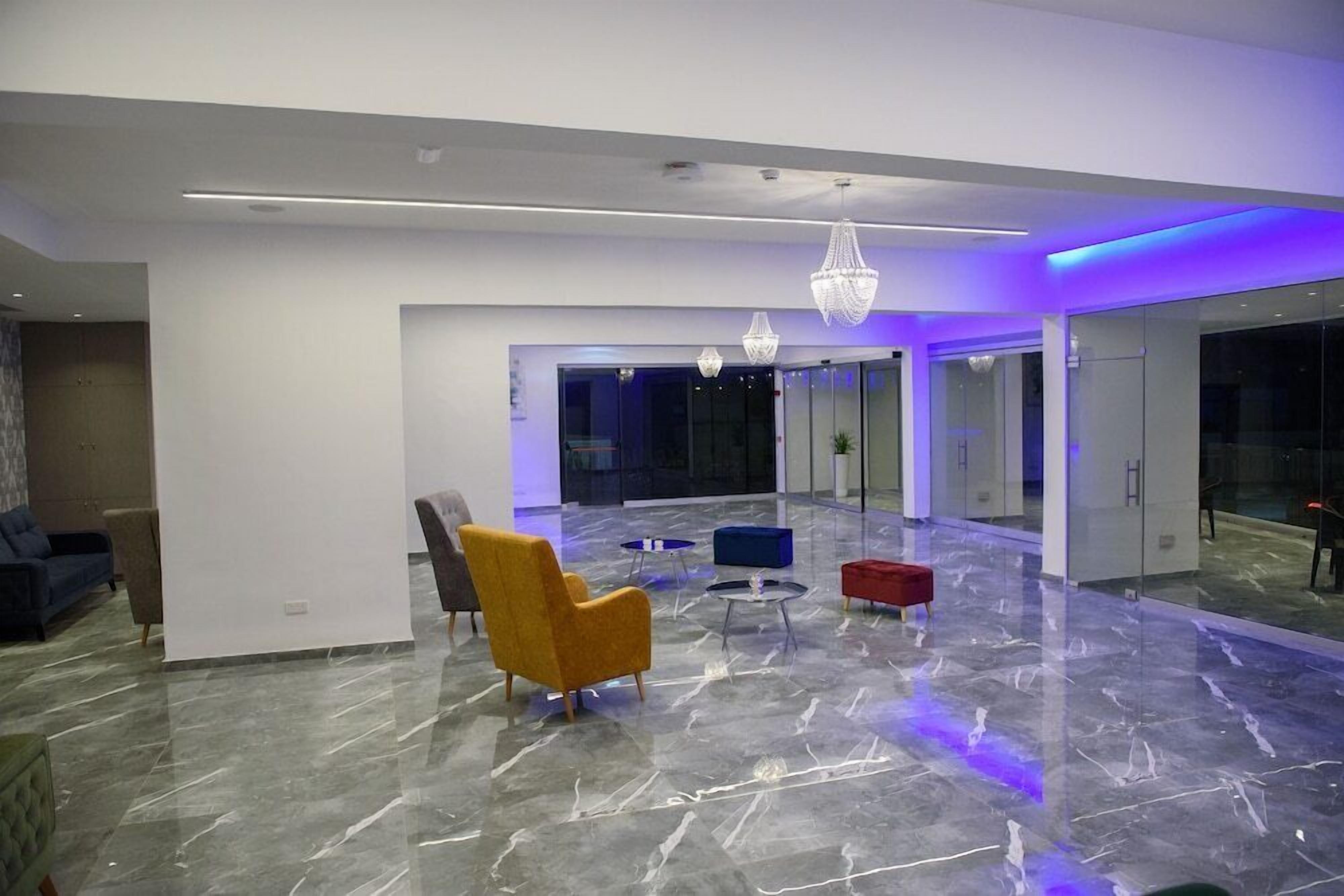Un hall d’entrée moderne avec un sol en marbre, un fauteuil jaune, un canapé bleu et un pouf rouge.