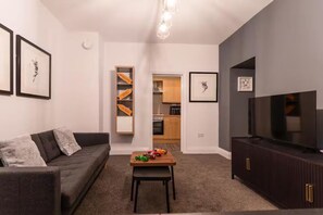 A living room with a grey sofa, a wooden coffee table with toys, a TV on a dark cabinet, and a kitchen in the background. - Cosy 1-bedroom apartment in Newport perfect for relaxing stays (Newport)