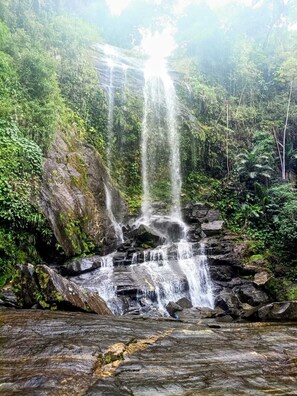 A waterfall cascading over rocks surrounded by lush greenery. - Angra Sol e Mar Suite: rest, comfort and enchanting beaches. Close to Brasfels. (Angra dos Reis)