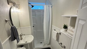 A compact bathroom with a toilet, sink, shower, and a small potted plant.