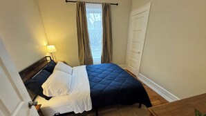 A bedroom with a bed, bedside table, lamp, window with curtains, and a door.
