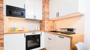 Una cocina compacta con armarios blancos, un horno negro, una pared de ladrillo y una encimera de madera.