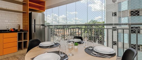 Un comedor con una mesa redonda dispuesta para cuatro personas, un refrigerador y vistas a un edificio a través de una barandilla de cristal.