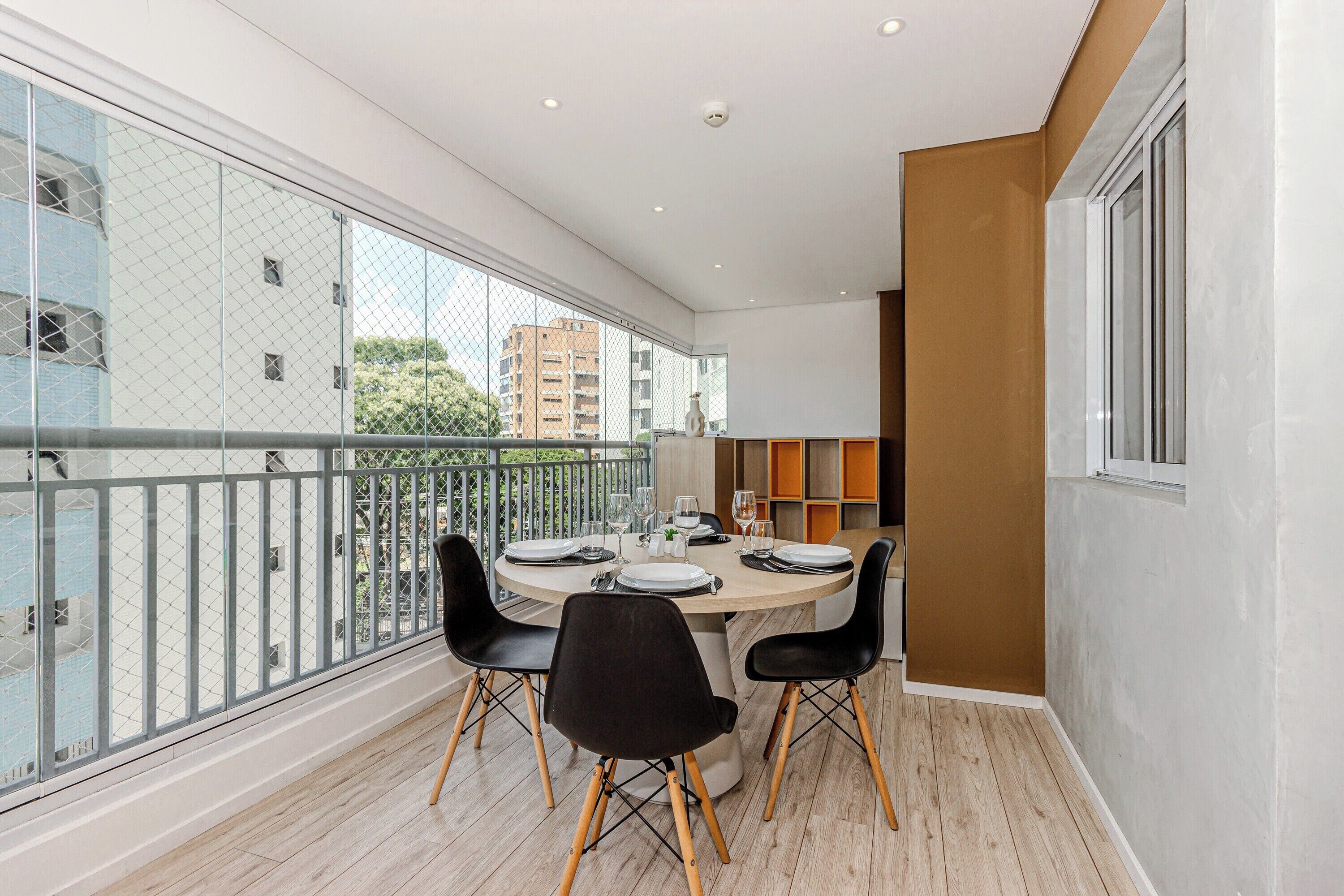 Uma varanda com uma mesa de jantar posta para quatro pessoas, rodeada por cadeiras pretas com pernas de madeira.