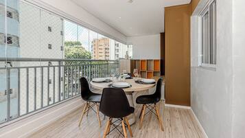 Uma varanda com uma mesa de jantar posta para quatro pessoas, rodeada por cadeiras pretas com pernas de madeira.