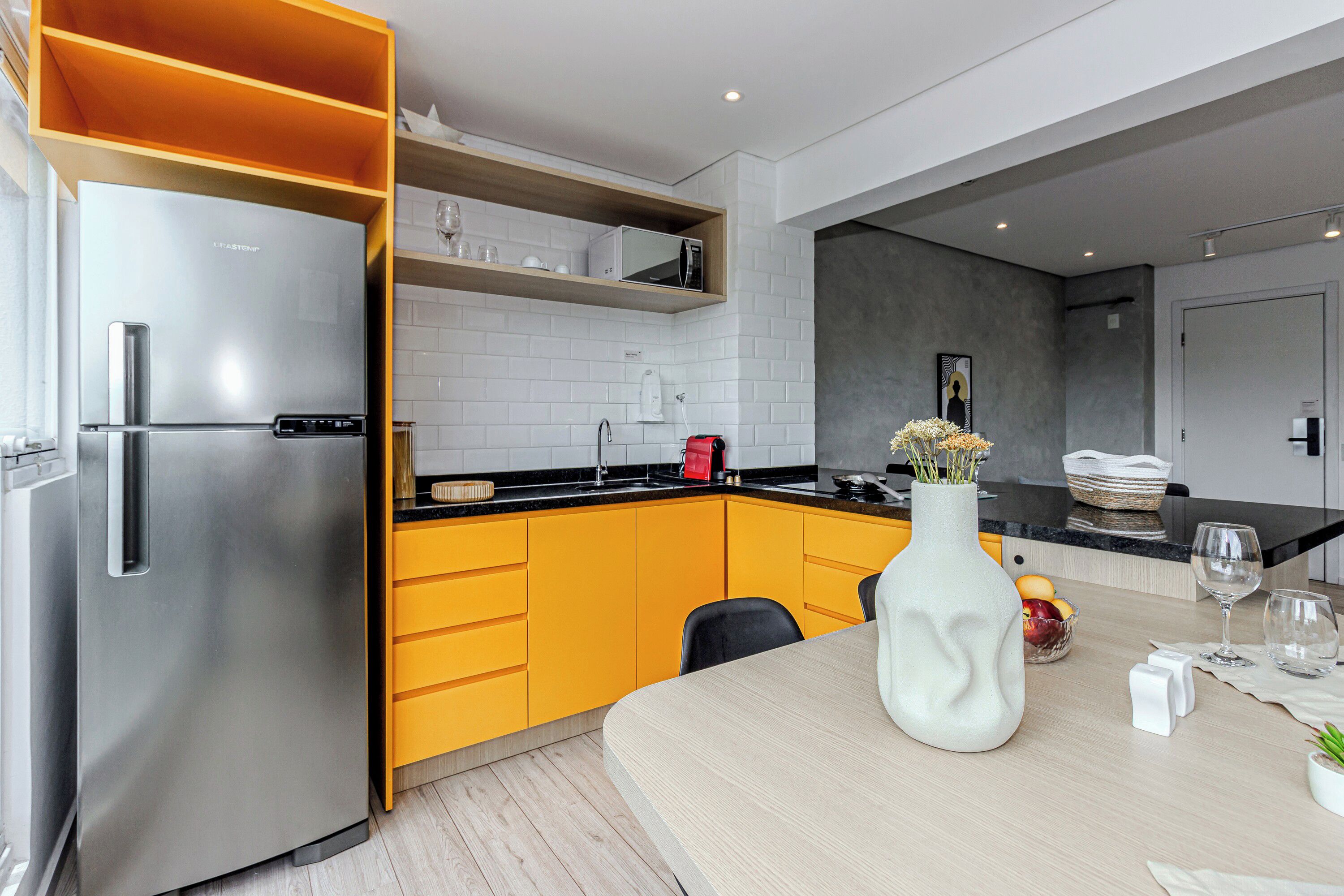 Une cuisine moderne avec un réfrigérateur en acier inoxydable, des armoires jaunes et une étagère en bois.