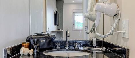 Un baño con lavamanos, espejo, secador de pelo y artículos de aseo.