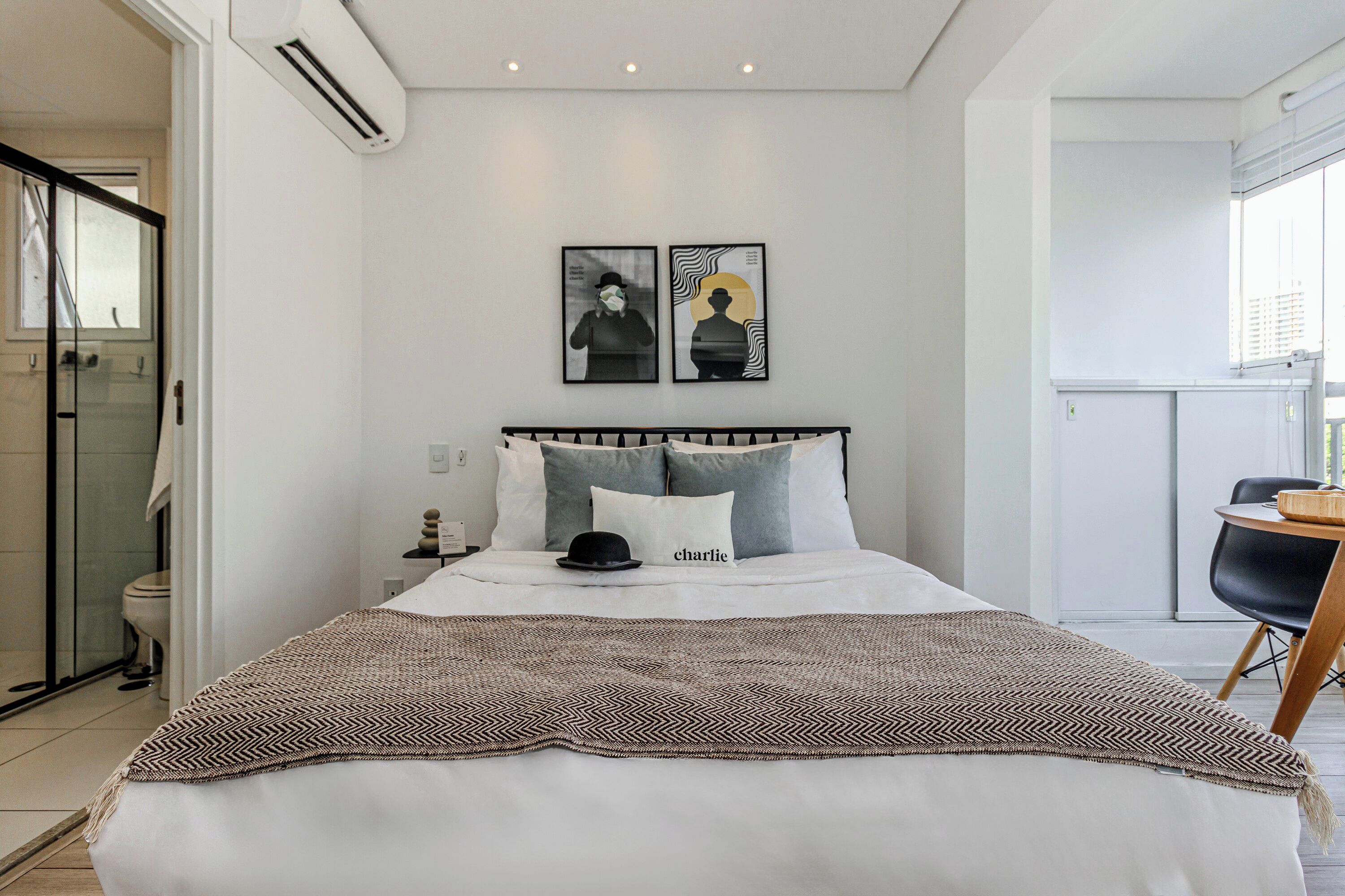Un dormitorio moderno con una cama grande, una mesita de noche y una silla. Hay una ventana con vistas a edificios.