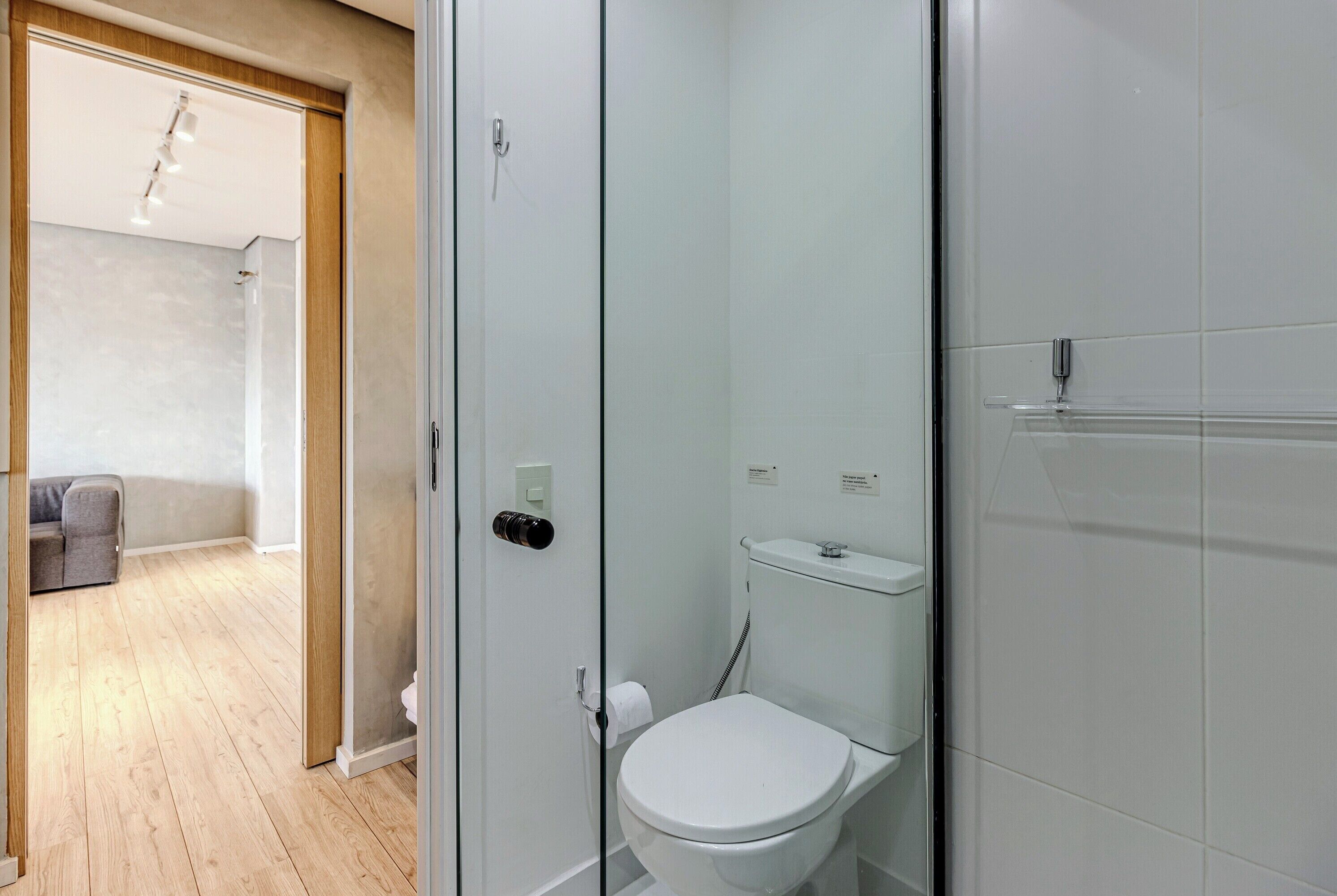 A modern bathroom with a toilet, shower, and glass door leading to a living area.