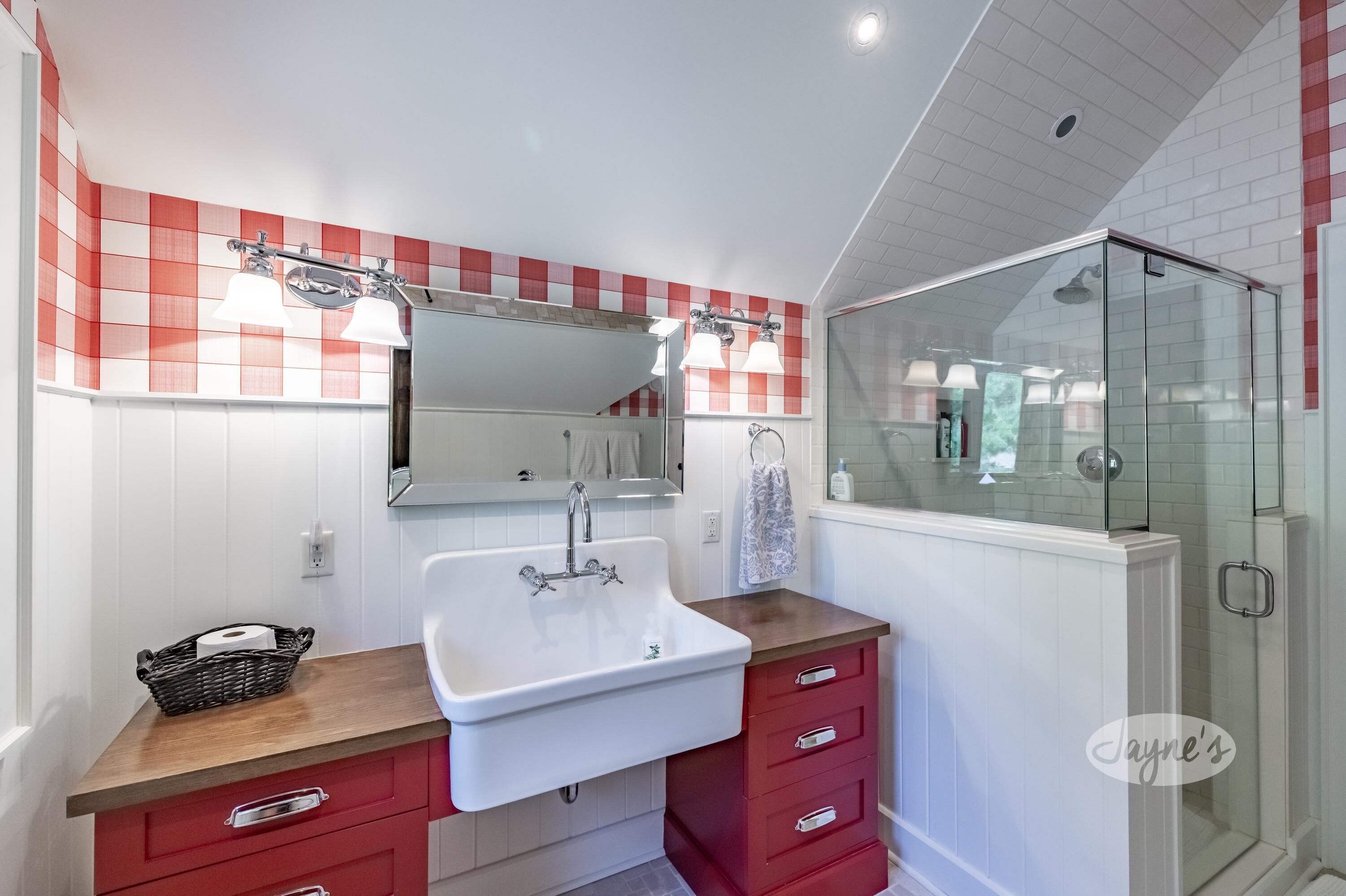 A bathroom with a white sink, red cabinets, a glass shower enclosure, and a red and white checkered wall.