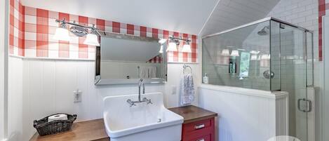 A bathroom with a white sink, red cabinets, a glass shower enclosure, and a red and white checkered wall.