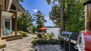 Een terras met een barbecue, buitenzitplaatsen en uitzicht op een meer.