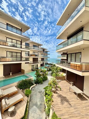Un moderno complejo turístico con varios balcones, una piscina central y exuberante vegetación.