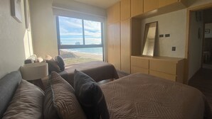 Ein Schlafzimmer mit einem großen Bett, zwei Nachttischen, einem Kleiderschrank und einem Fenster mit Blick auf den Strand.