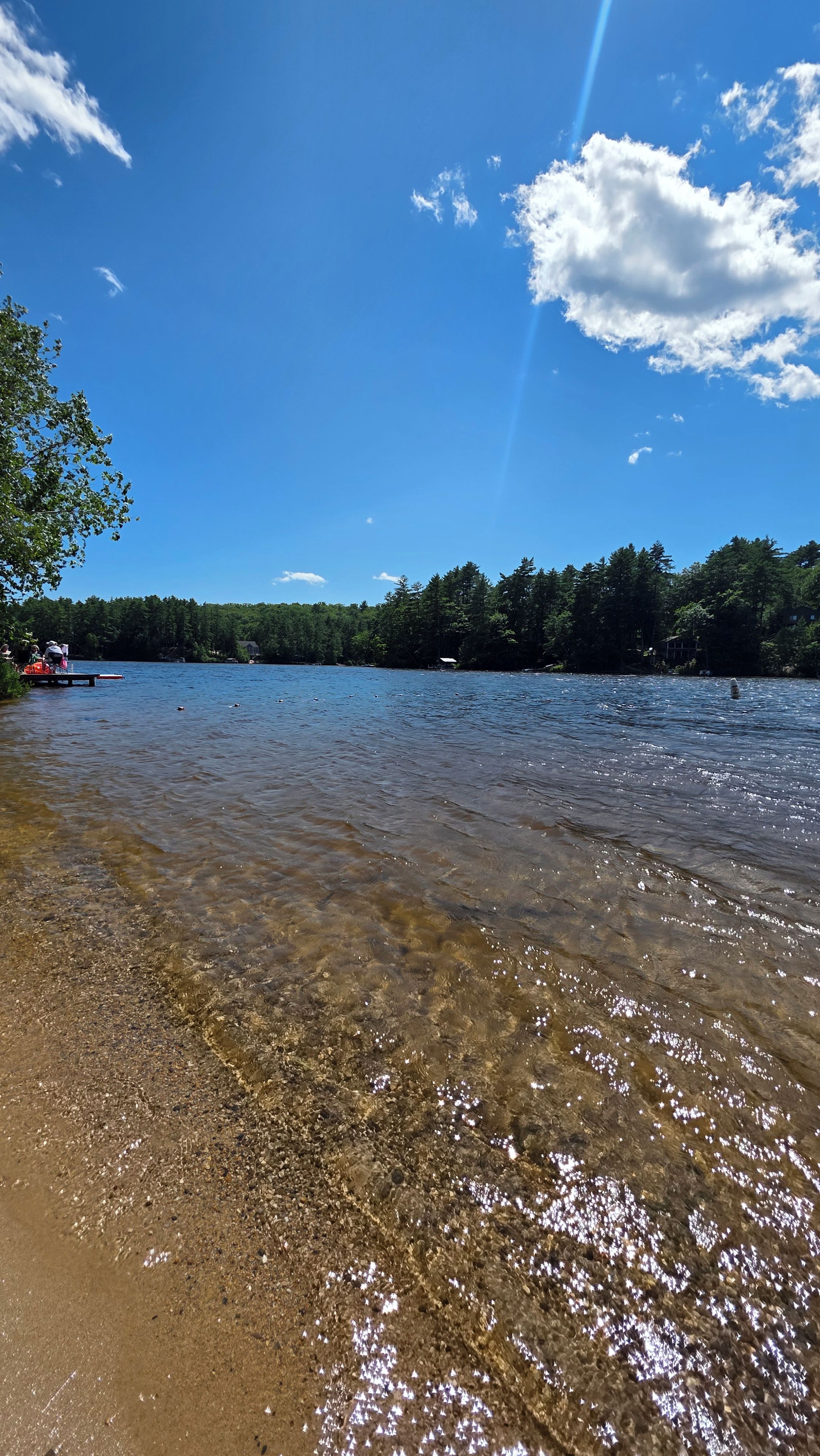 Un lac aux eaux limpides, bordé d’une plage de sable, entouré d’arbres et surplombé d’un ciel dégagé.