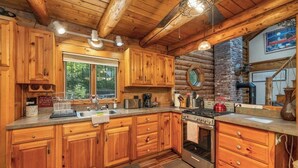 A rustic cabin kitchen with wooden cabinets, a large window, a stove, and a brick wall. - Charming year round lake view cabin! (Wakefield)
