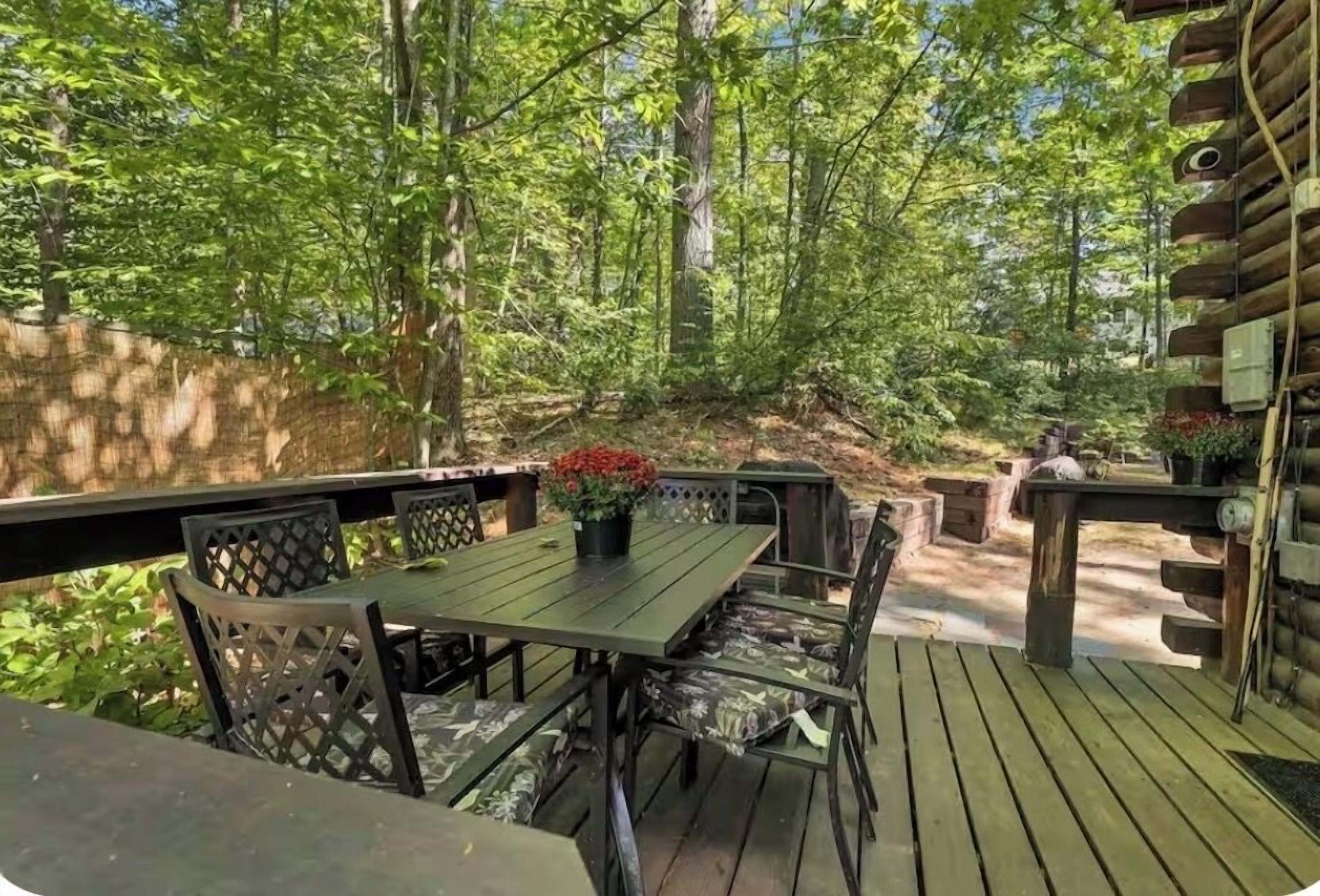 A wooden deck with a table and chairs, surrounded by trees.