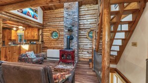 A log cabin interior with a fireplace, wooden furniture, and a loft area. - Charming year round lake view cabin! (Wakefield)