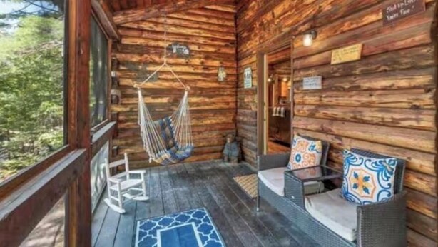 A log cabin with a hanging chair, wicker furniture, and a view of the outdoors. - Charming year round lake view cabin! (Wakefield)