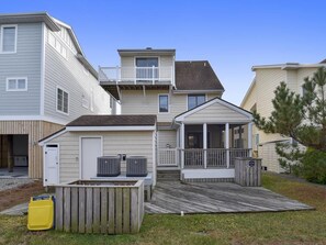 Um edifício residencial com vários andares, uma varanda coberta, um pequeno deck e uma garagem visível.