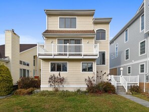 A multi-story residential building with a balcony on the second floor, a front porch, and a small front yard with shrubs. - 5 Bedroom Beach House w/ Pool, Gym & Tennis Access (Bethany Beach)