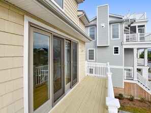 A residential building with a covered porch, sliding glass doors, and a second-story balcony. - 5 Bedroom Beach House w/ Pool, Gym & Tennis Access (Bethany Beach)