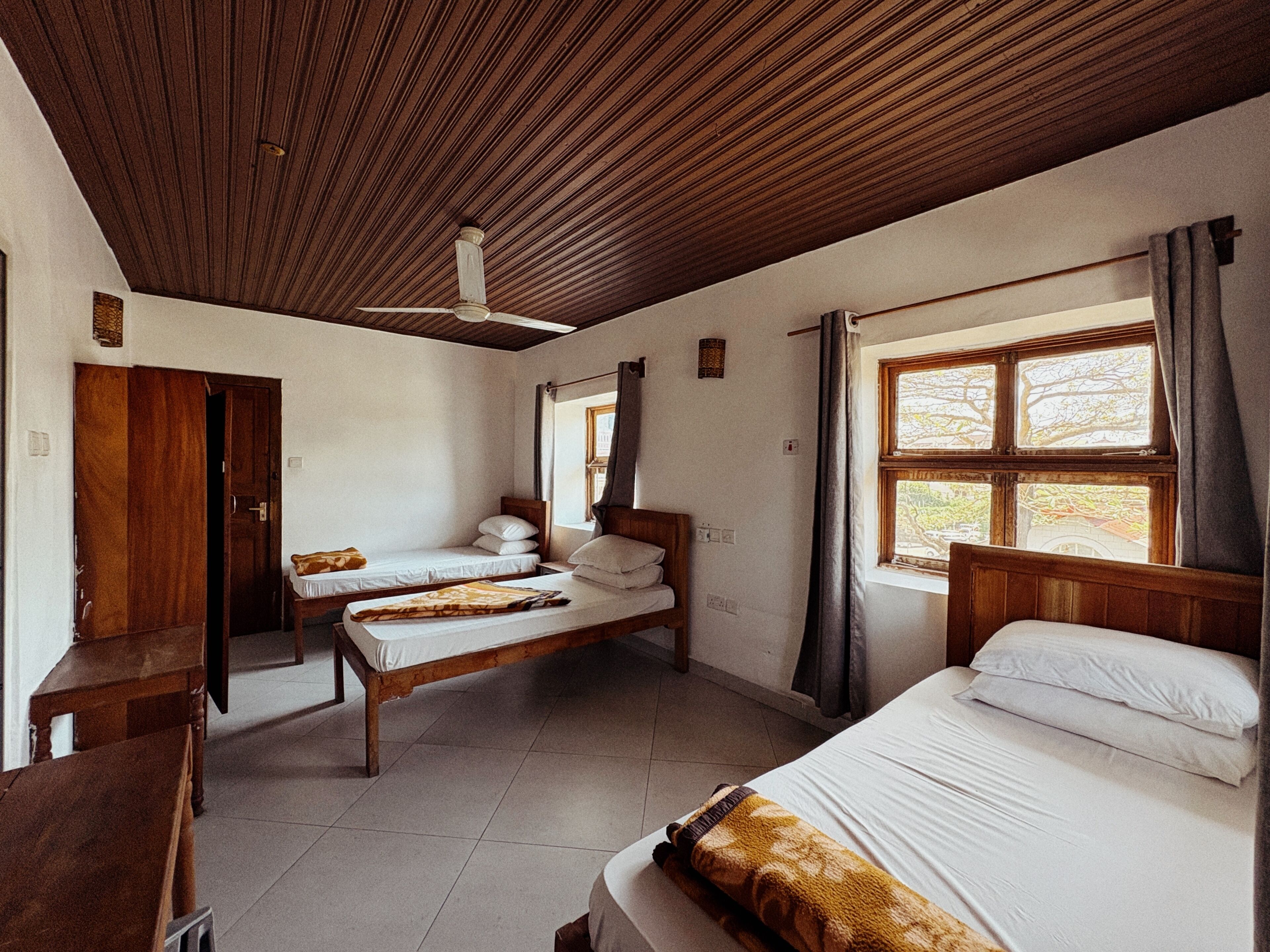 Een kamer met twee bedden, een houten plafond, een raam met gordijnen en een deur.