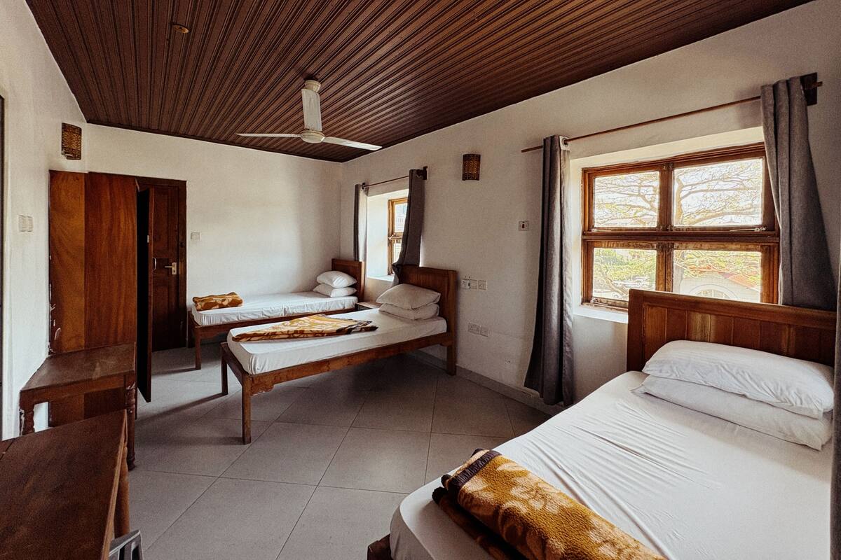 Une chambre avec deux lits, un plafond en bois, une fenêtre avec des rideaux et une porte.