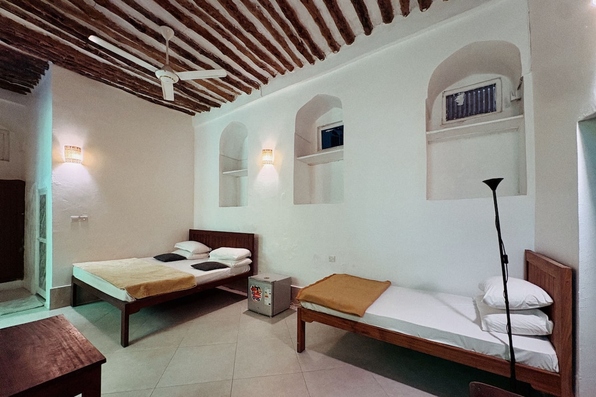 Une chambre avec deux lits, un plafond en bois et des lampes fixées au mur.