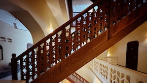 Een houten trap met gedetailleerde open structuren, die leidt naar een lager gelegen niveau met een sierlijk hekwerk en een brandblusser.